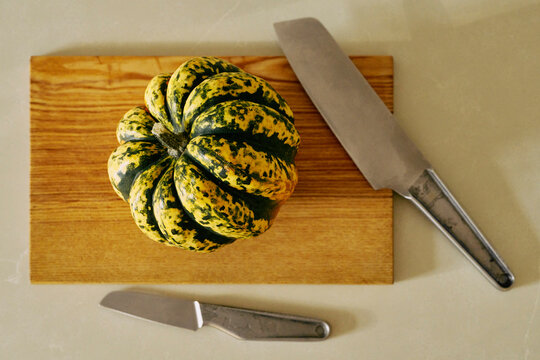 Still life view from above of acorn squash on wooden cutting board with knife
