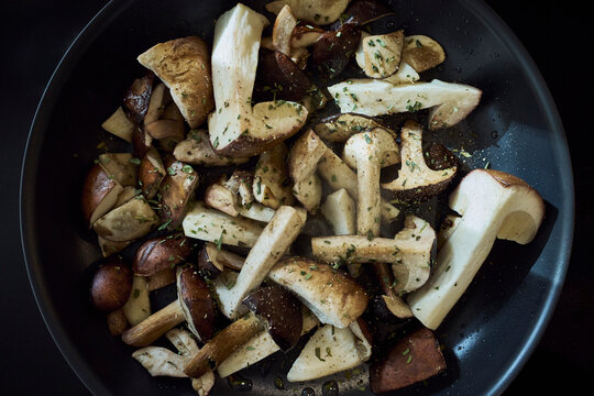 View from above of fresh porcini mushrooms sauteeing with herbs in cooking pan
