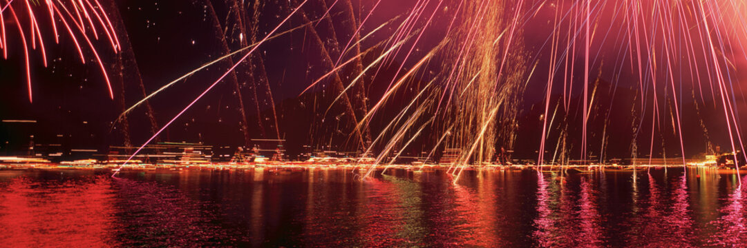 Panoramic view of vibrant red and yellow fireworks in night sky above Traunsee Lake, Austria
