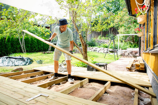 Man building wooden deck in backyard. Authentic DIY home improvement project during summer. Outdoor house renovation and construction.