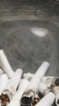 Vertical video. Dolly slider, close up. Close-up view inside a glass jar filled with cigarette butts, highlighting the health risks and environmental impact of smoking, with visible ashes and burnt fi