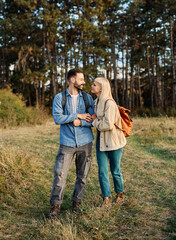 Fototapeta premium Hiking couple, young man and woman enjoys nature with trekking poles in a lush forest during a sunny day