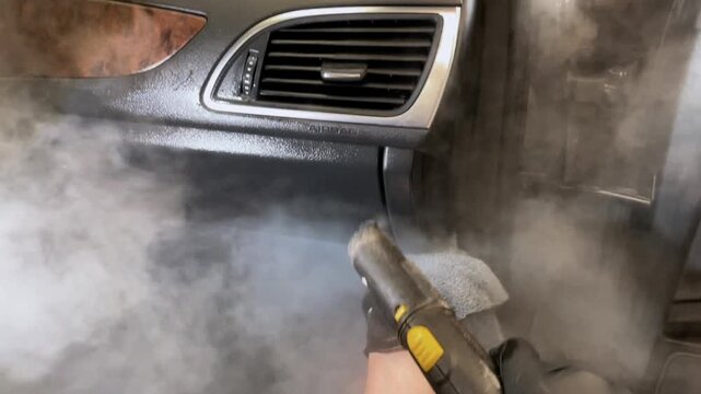 Car detailing and the concept of car interior care. The detailing master cleans the car interior with a hot steam cleaner close-up. Dry cleaning of the car interior, close-up, selective focus. 