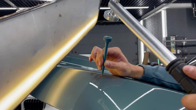 PDR. Process of paintless dent repair on car body. The mechanic at the auto shop with tools to repair dents in car body. Body repair. A specialist repairs a dent on the car body without painting.