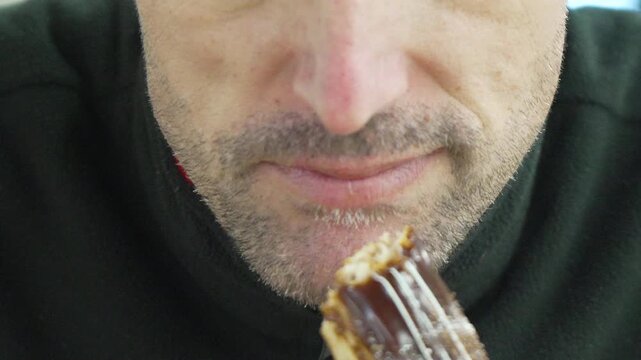 Man eating pastry and drinking coffee during a break indoors enjoying a delicious chocolate eclair dessert