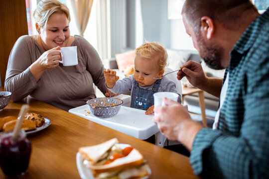 Smiling parents feeding messy toddler breakfast at home