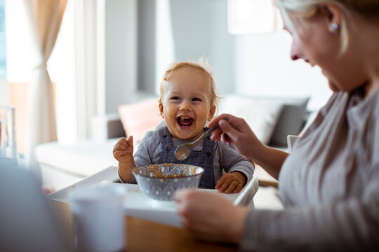Mother feeding laughing baby at home