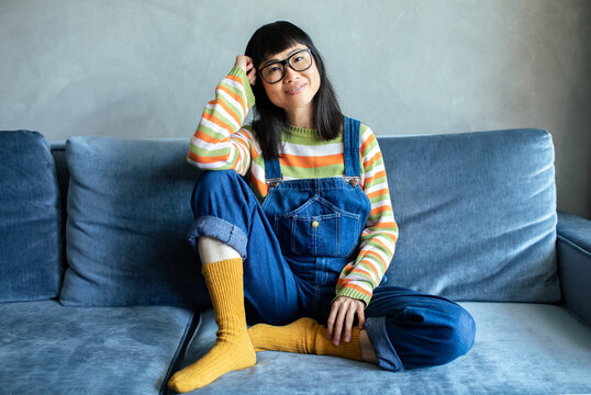 Smiling young woman in overalls relaxing on sofa at home