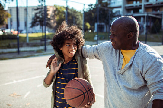 Smiling man and boy with basketball on outdoor court