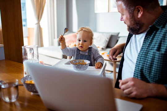 Father working from home while toddler eats breakfast