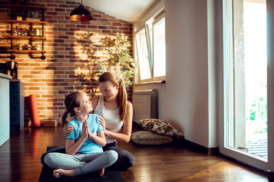 Mother and daughter meditating on yoga mat at home