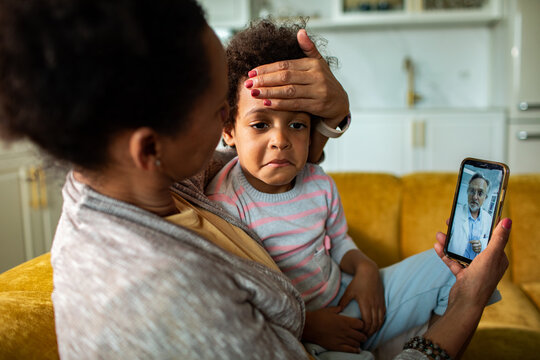 Parent comforting sick child during telehealth visit at home