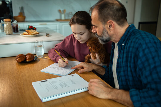 Father helping daughter with homework at kitchen table