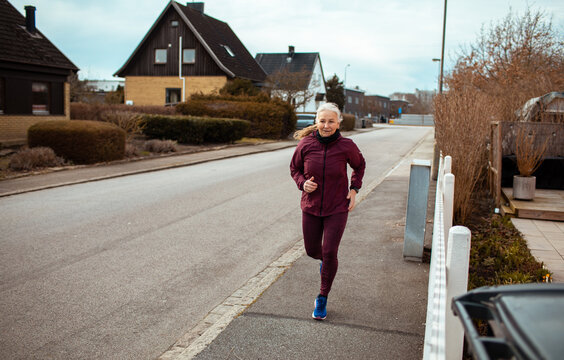 Senior woman jogging on suburban street in cold weather