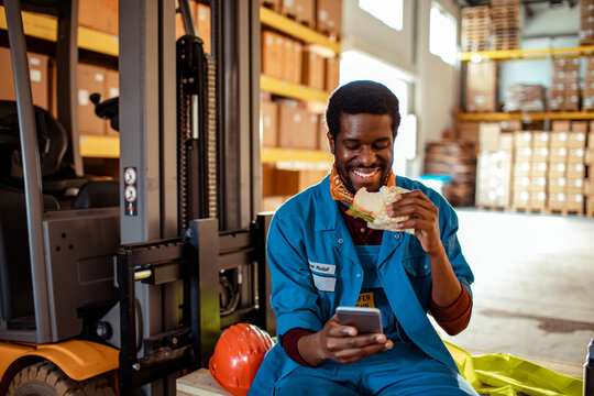 Warehouse worker eating sandwich and using smartphone during break