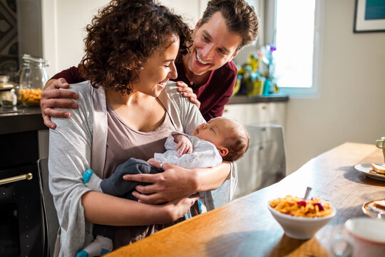 Parents cuddling newborn baby in home kitchen
