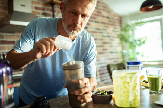 Middle aged man preparing protein shake in home kitchen