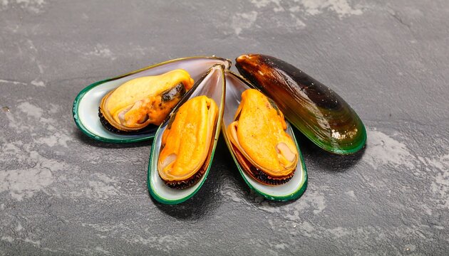 Close-up shot of cooked mollusks in their open shells, revealing the orange and yellow flesh. The shells have a vibrant green rim