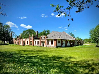 Obraz premium Abandoned Kazokine Manor in Lithuania showcases a deteriorating yet picturesque brick structure with arched windows and a tiled roof. Nestled in a sprawling grassy field