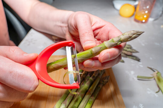 Peeling asparagus with a vegetable peeler over a cutting board in a kitchen environment. Concept of cooking process, food preparation workflow