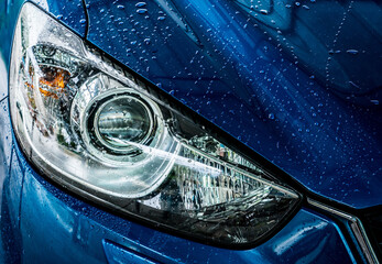 Closeup headlamp of blue car are washing with water. Car care service business concept. Car wash service. Car covered with drops of water after cleaning with high pressure water spray. Auto care. © Fahroni