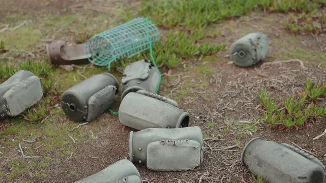 Abandoned fishing floats and plastic trap lying on sandy ground with coastal vegetation