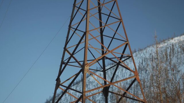 Power line towers stand tall among trees in this location. The camera shows different views of the towers against the blue sky. Birds can be seen flying around the towers.