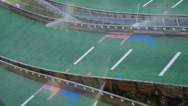 A beautiful rainbow forms in the mist of water as automated sprinklers spray the plastic mat of a ski jumping hill. Cinematic 4K 29.97fps slow motion detail.