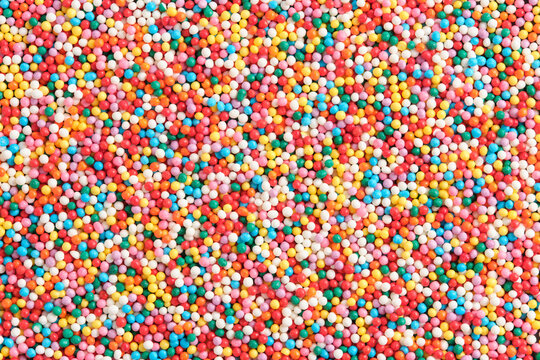 High resolution background thousands tiny, multi colored sugar nonpareils, creating vibrant and chaotic rainbow texture.