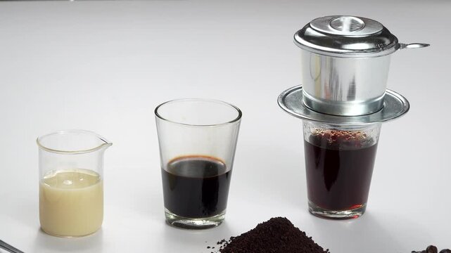 Wide shot of Vietnamese coffee ingredients including condensed milk, black coffee, and an active phin filter on a white background. Premium recipe footage.