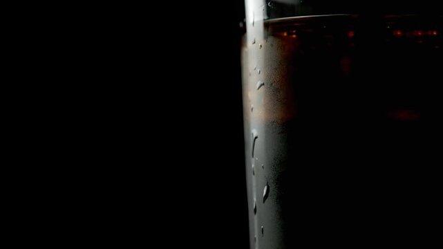 Glass with whiskey and ice cubes in it, alcoholic drink on black background
