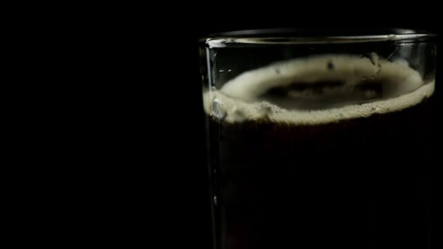 Two ice cubes are dropped into a glass of soda on a black background, space for text