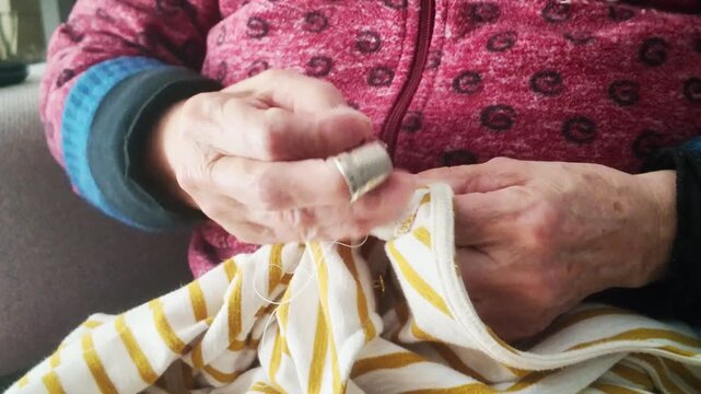 Elderly woman's wrinkled hands mending fabric