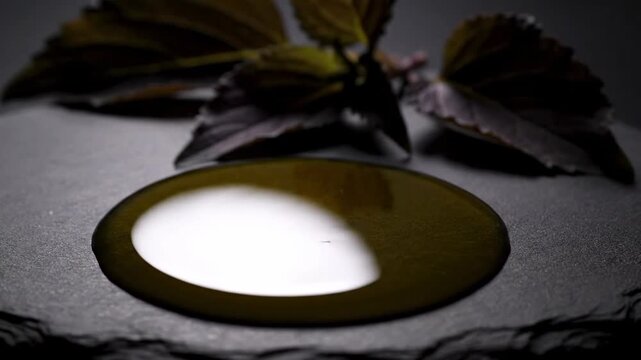 Olive oil pouring onto dark slate surface with basil leaves in background