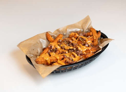 Plate of loaded fries with cheese, meat, and onions served in a black basket on a white table