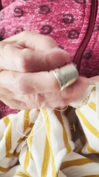 Elderly woman's wrinkled hands mending fabric