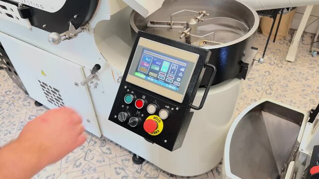 Professional Roaster Operator Setting Up Industrial Coffee Roasting Machine Using Digital Touchscreen Interface Over The Shoulder View inside Specialty Roastery Production Facility with Human Hand