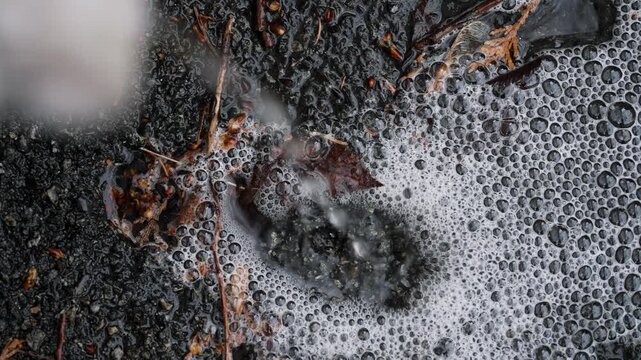 Close-up of rainwater dripping from house drainage pipe into puddle on ground. Water drops creating ripples on wet surface during rainy weather, with soft blurred background and shallow shallow depth 