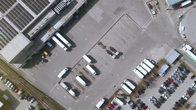 An aerial view shows a bustling distribution warehouse with numerous trucks lined up along the expansive driveway. Vehicles navigate the loading and unloading zones, highlighting.