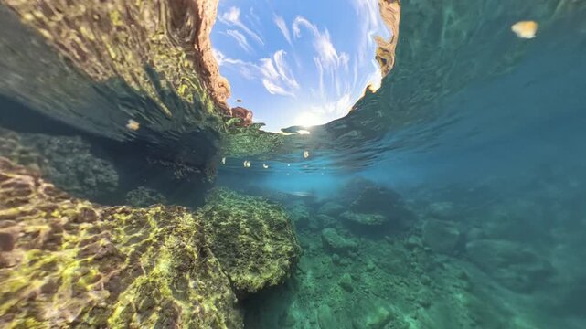 Wide underwater view of rocky formations with sunlight shining down from the surface, capturing a serene marine landscape with floating bread crumbs