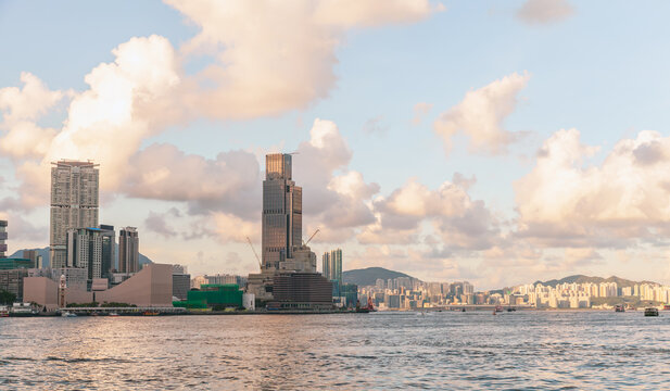 Warm sunset light bathes Hong Kong Harbour skyline, highlighting modern high‑rises, calm water and soft clouds. A peaceful urban seascape