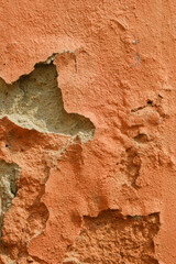 Fototapeta premium Vertical close up of a weathered orange exterior wall showing heavy texture, peeling paint layers, and crumbling concrete. Ideal for industrial grunge or vintage architectural backgrounds