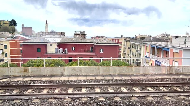 Ligurian regional train window view passing Recco townscape. Sunny day journey through Italian Riviera showing traditional colorful apartments, San Rocco church and Mediterranean sea in distance