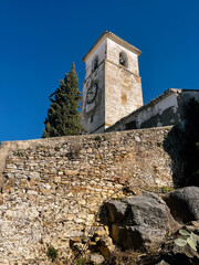 Old white church tower behind a stone wall under a clear blue sky. Colmenar, Malaga, Andalusia, Spain.
