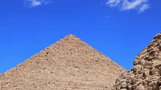 Close-up view of Pyramid of Menkaure with subsidiary pyramids and ancient stone ruins at Giza, Egypt. Massive limestone blocks against vivid blue sky. Travel and history.