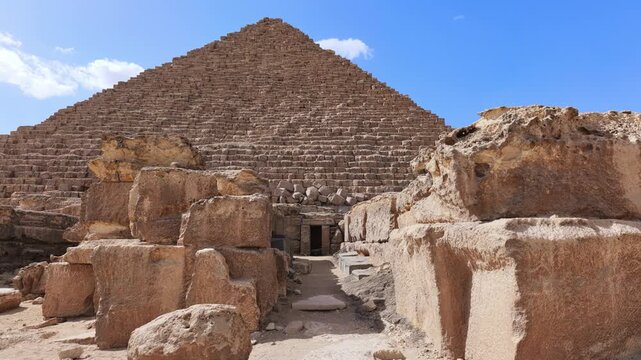 Pyramid of Menkaure with mortuary temple entrance and massive granite blocks in foreground at Giza, Egypt. Ancient archaeological site under blue sky. Travel and history.