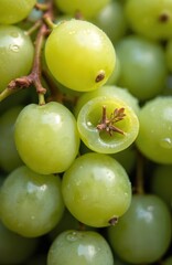 Fototapeta premium Close-up of seedless green Shine Muscat grapes with water droplets. One grape is cut, revealing its juicy interior and stem structure. Fresh, ripe fruit creates a vibrant background.