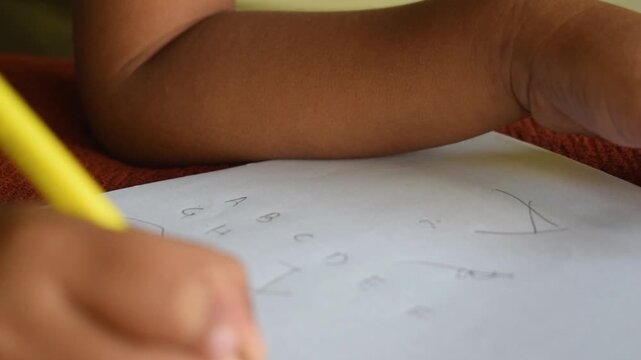 Close up of a child hand holding a yellow pencil and drawing on paper at home or school, concept of education, teaching, creativity, learning, self development and skill building.