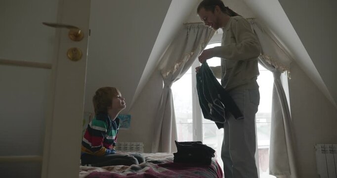 Man puts warm clothes on child. Dad help child to dress at home. 4K 10-bit