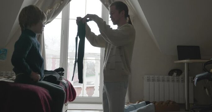 Man puts warm clothes on child. Dad help child to dress at home. 4K 10-bit